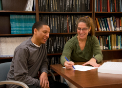 Smiling female professor points to biostatistical equation on a piece of paper with male MPH student