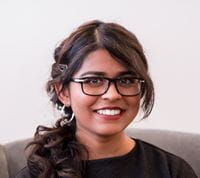 Krithika Prakash smiles at the camera, standing against a white background.