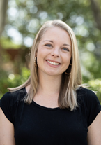 Carly is wearing a short sleeve black shirt. She has shoulder length blonde hair and is smiling at the camera.