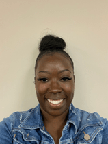 Tiarra is wearing a blue jean jacket. She has her black hair pulled into a top bun, has a small nose piercing, and is smiling.