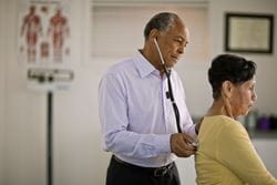 male physician listening through stethoscope on female patient's back