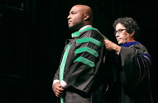 Photo of faculty member placing academic hood on graduating student