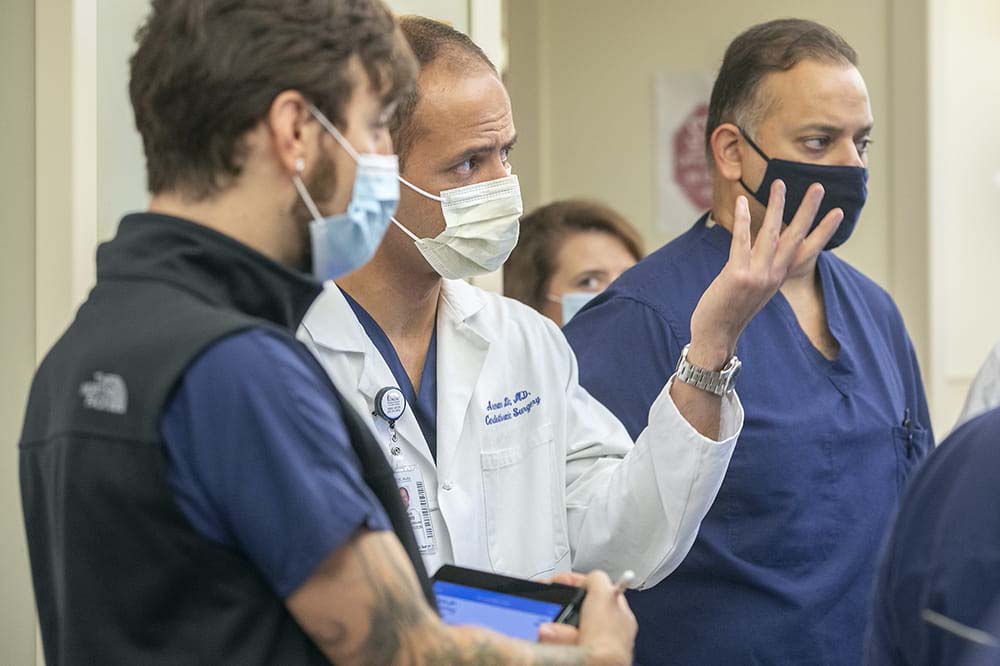 Dr. Arman Kilic gestures while wearing a white lab coat and a surgical mask.