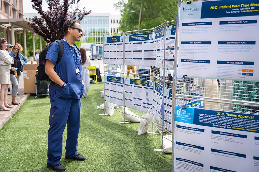 A man wearing blue scrubs looks at a series of posters that are as tall as he is.