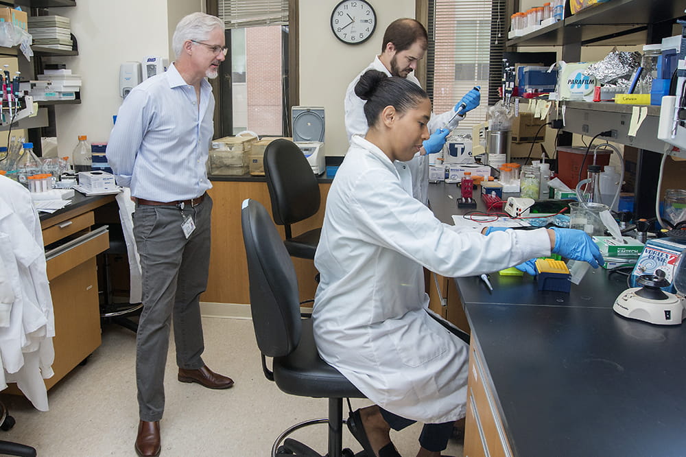 Chris Cowan, chairman of the Department of Neuroscience, observes Adam Harrington and Catherine Bridges at work. Harrington and Bridges are joint lead authors of a new paper about MEF2C haploinsufficiency syndrome.